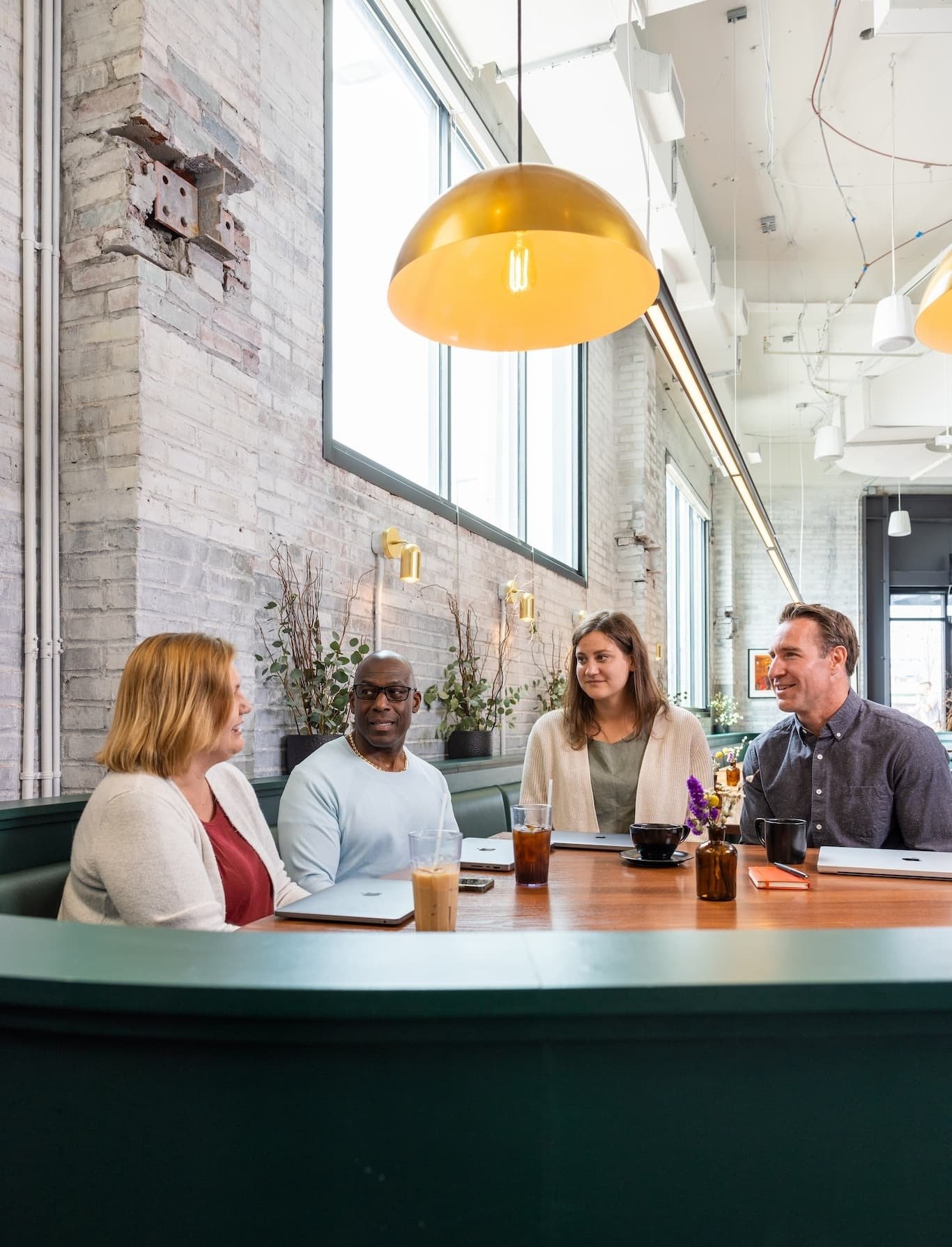 Four people sit around a well-lit table in a coworking space, laptops all around.