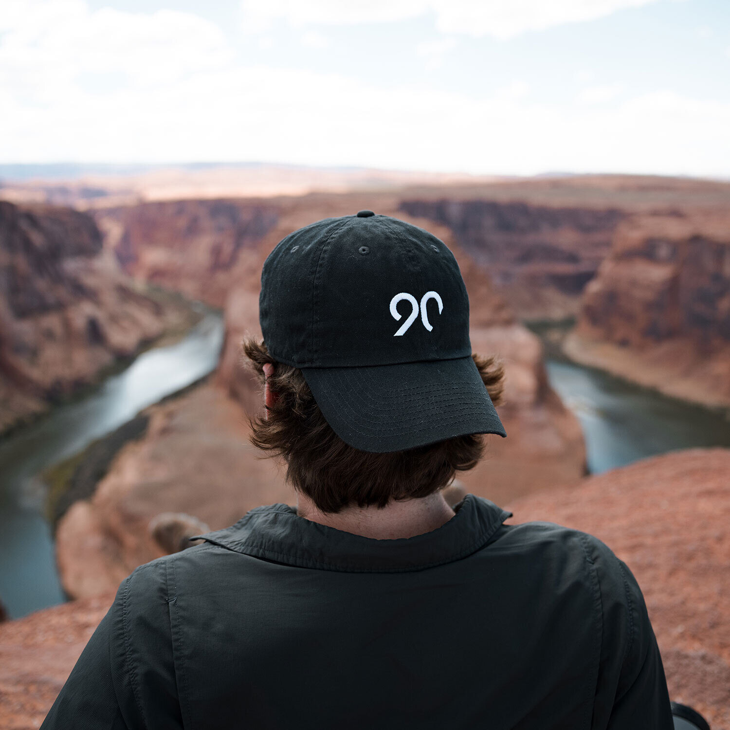 A Ninety employee wearing a 90 cap, seated in front of a canyon and river