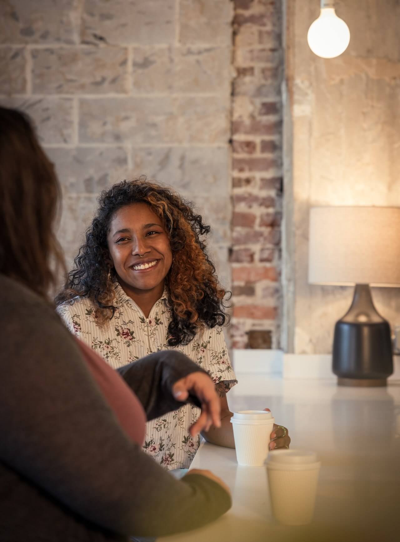 Two employees sitting at a coffee bar chatting and smiling.
