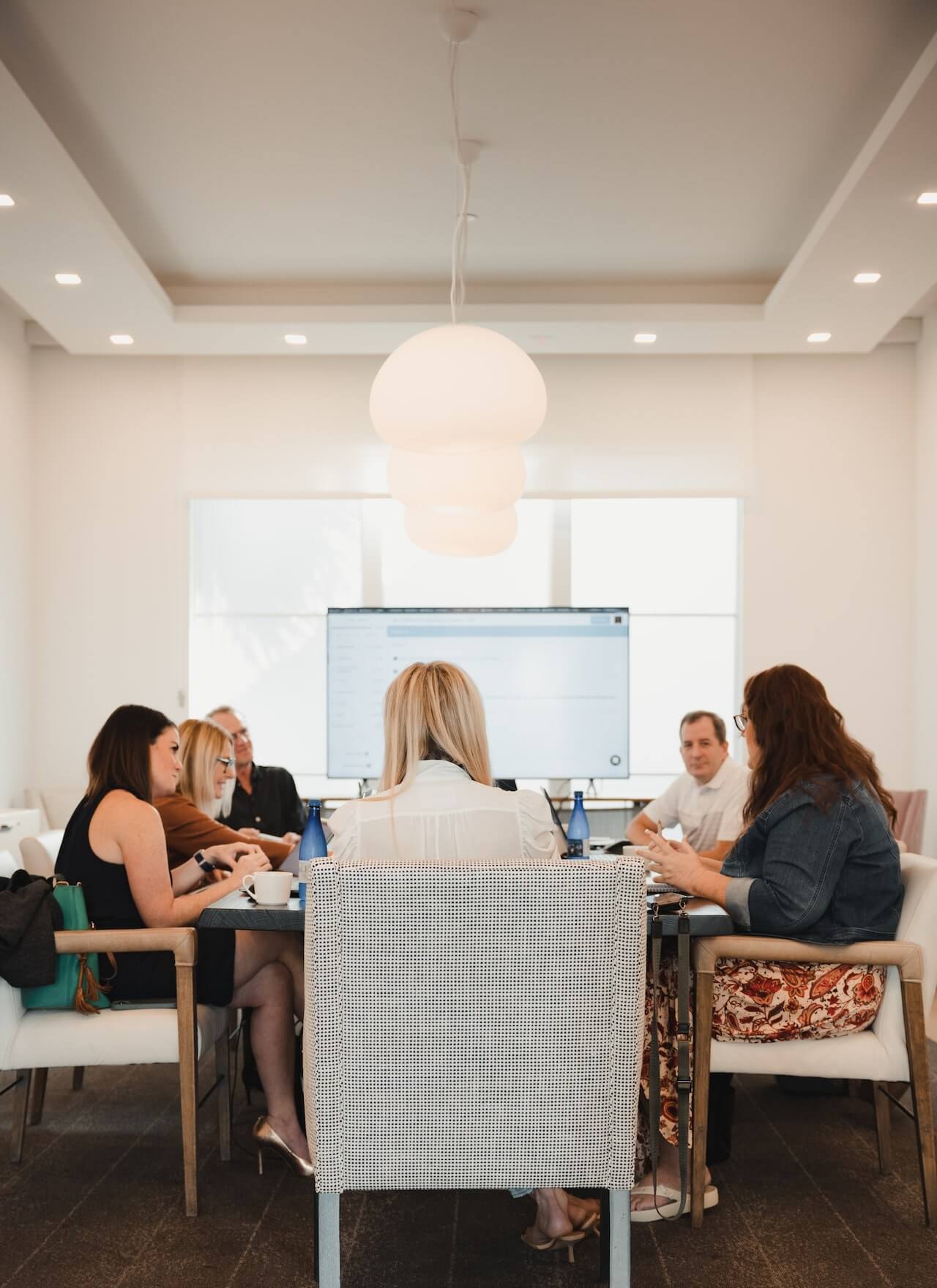 Employees seated around a table having a discussion around a table. Display screen in the background.