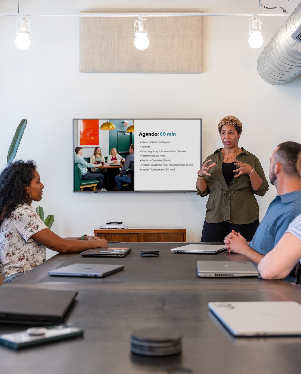 An employee giving a presentation with slide deck to a table of colleagues.