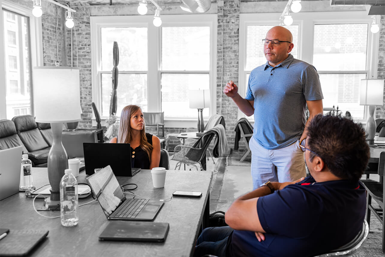 In an office, a man presents EOS coaching strategies, capturing the attention of his colleagues during the meeting.