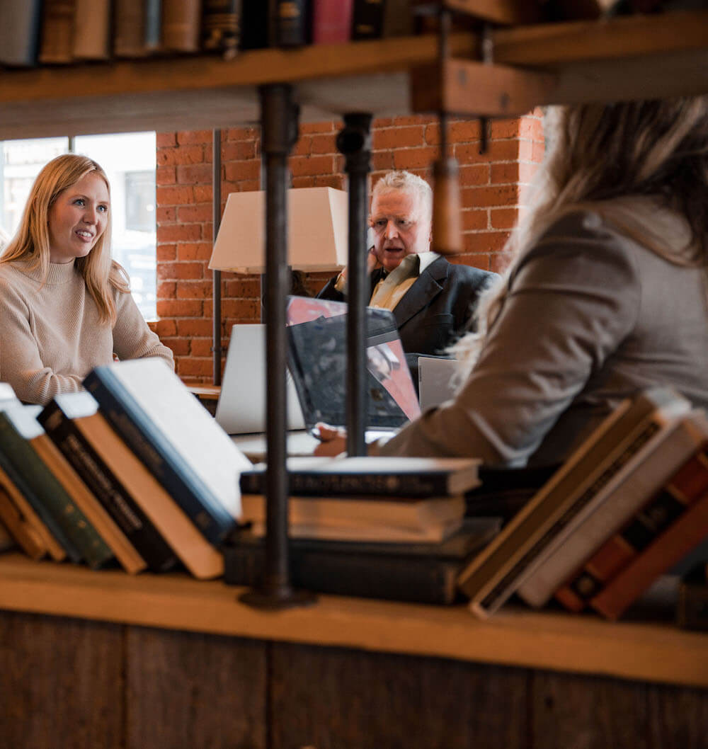 Three employees in a meeting near a bookshelf having casual conversation.