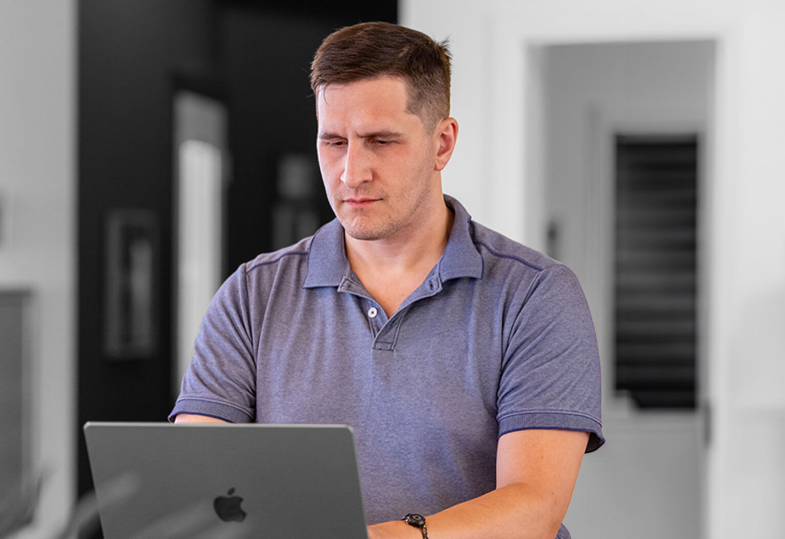 A man seated at a desk, focused on his laptop, surrounded by a tidy workspace.